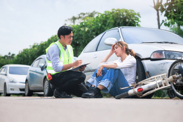Accident, crash or collision of auto car, bicycle at outdoor. Include asian people i.e. insurance officer man to examining, write document report and young girl or bicycle rider to injury on road. Concept for vehicle crash, insurance claim, emergency and safety.